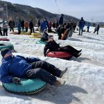 People tubing in snow with people standing behind them