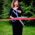 Woman in black dress cutting red ribbon with large scissors