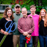 Family posing with red ribbon and scissors