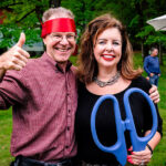 Couple posing with soman holding large scissors and man with red ribbon around forehead like a bandana