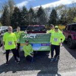 Five Mauch Chunk Trust Co. employees in bright neon yellow sweatshirts standing behind a pick up truck with an MCT banner on the tailgate