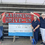 Carbon Chamber employees (three women) posing next to Mahoning Drive In marquee sign on stage