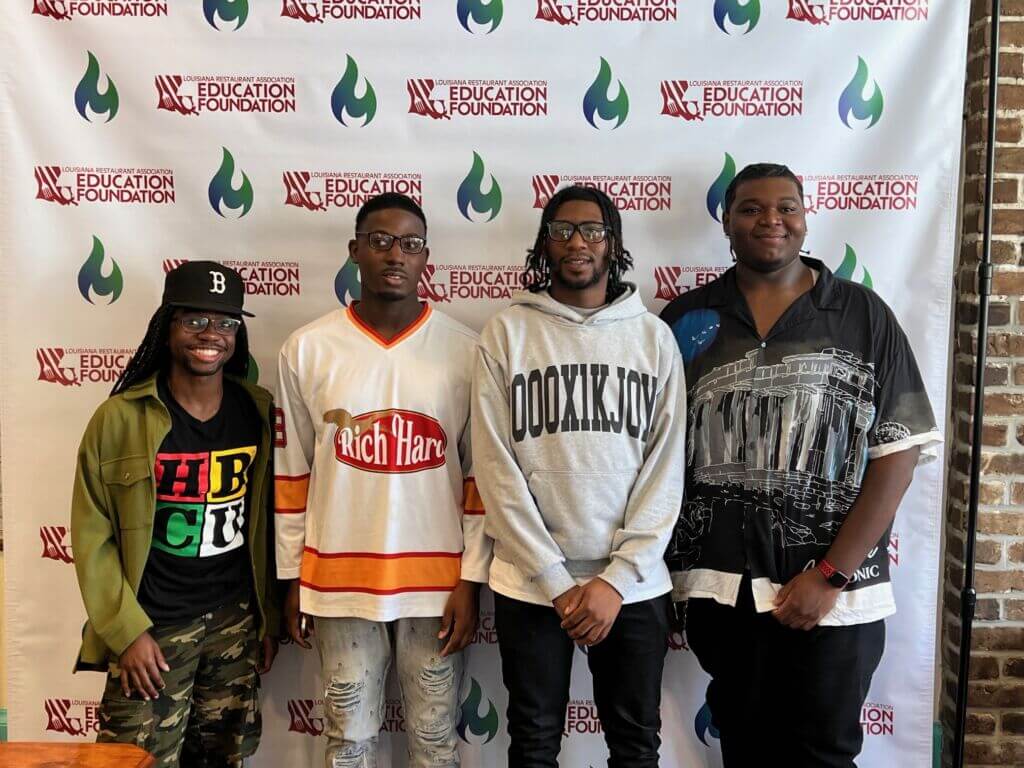 4 African American Young Men Standing in front of a Louisiana Restaurant Association Education Foundation Step and Repeat Banner