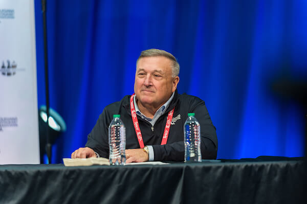 President and CEO of the Louisiana Restaurant Association seated at a table with water bottles on table. Blue background.