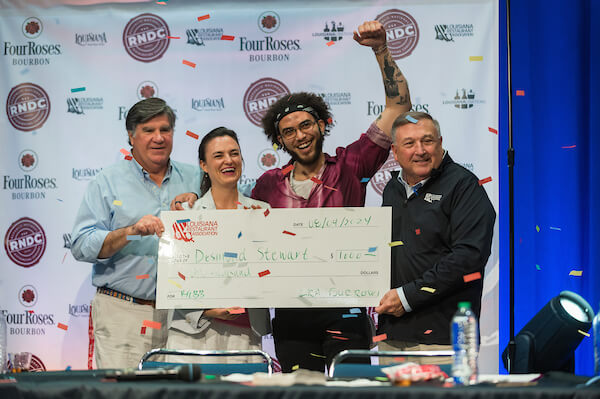 Three men and a woman holding oversized check. Confetti falling