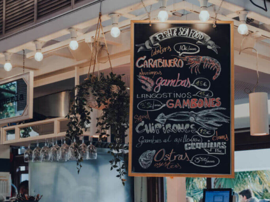 Indoor seafood market counter with hanging lights and a chalkboard menu.