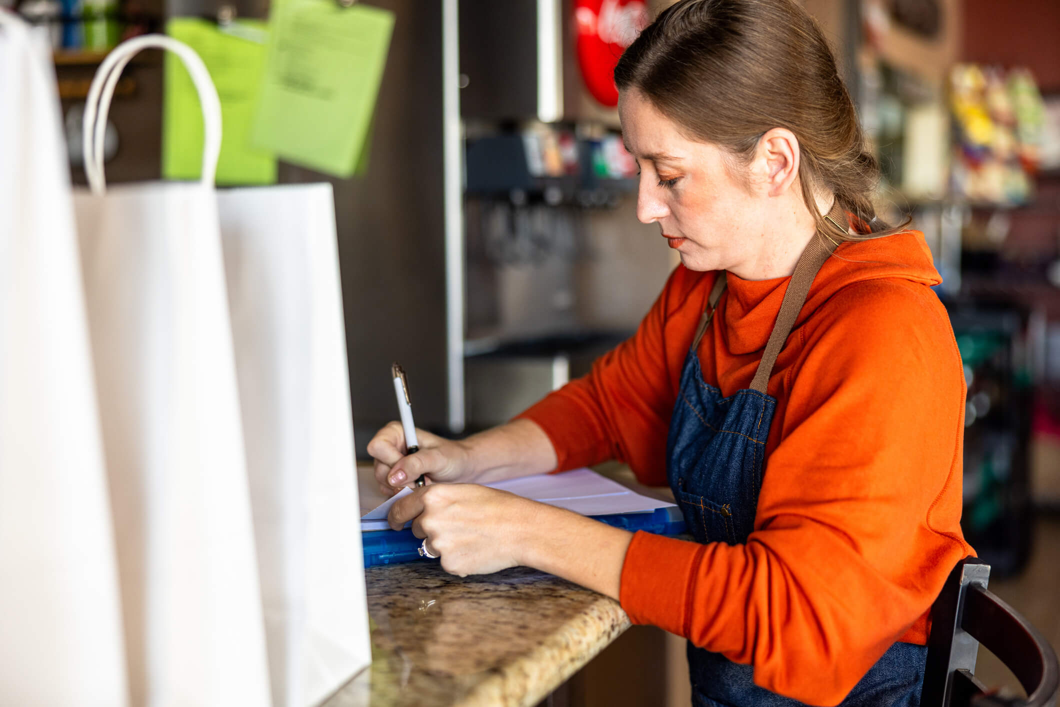 White femal brown hair wearing orange shirt and overalls signing a document