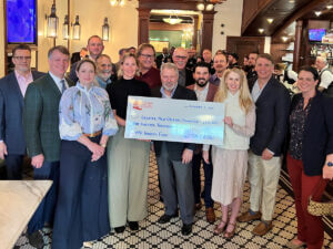 A group of people in a bar holding a large ceremonial check.