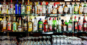 A well-stocked bar displaying various bottles of spirits along with an array of wine glasses and decanters on a shiny surface.