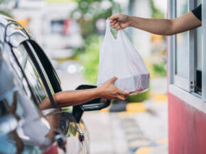 A drive-thru transaction with a person in a car receiving a plastic bag from a window in a red building.