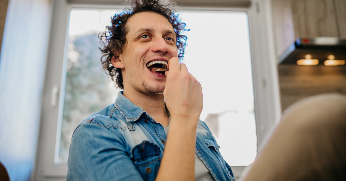 Person smiling while eating chocolate in a kitchen.