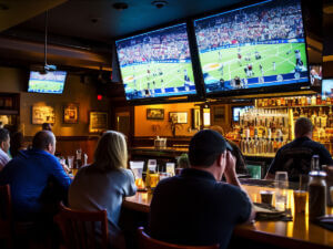 Patrons in a bar watching a football game on multiple large TVs above the bar counter.