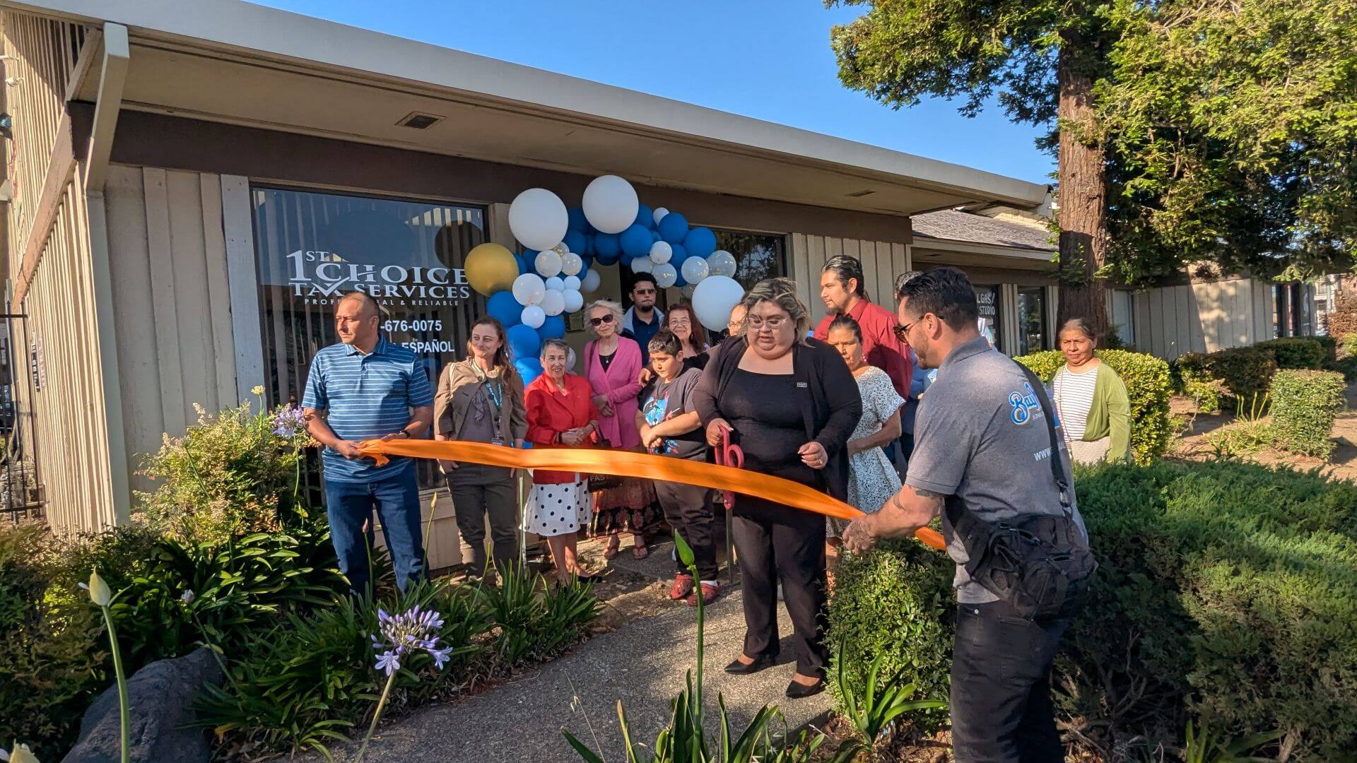 1st choice ribbon cutting 1920x1080 Esmeralda, owner of 1st Choice Tax Services, prepares to cut an orange ribbon outside her office in Fairfield during a ribbon-cutting ceremony surrounded by community members and supporters.