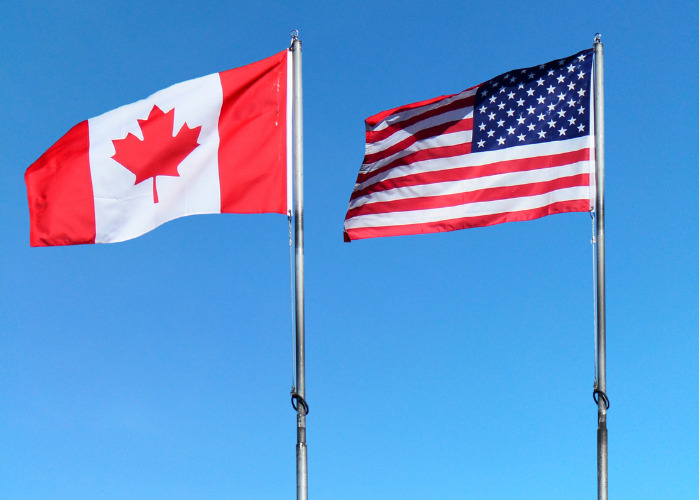 Canada and U.S. flags against blue sky