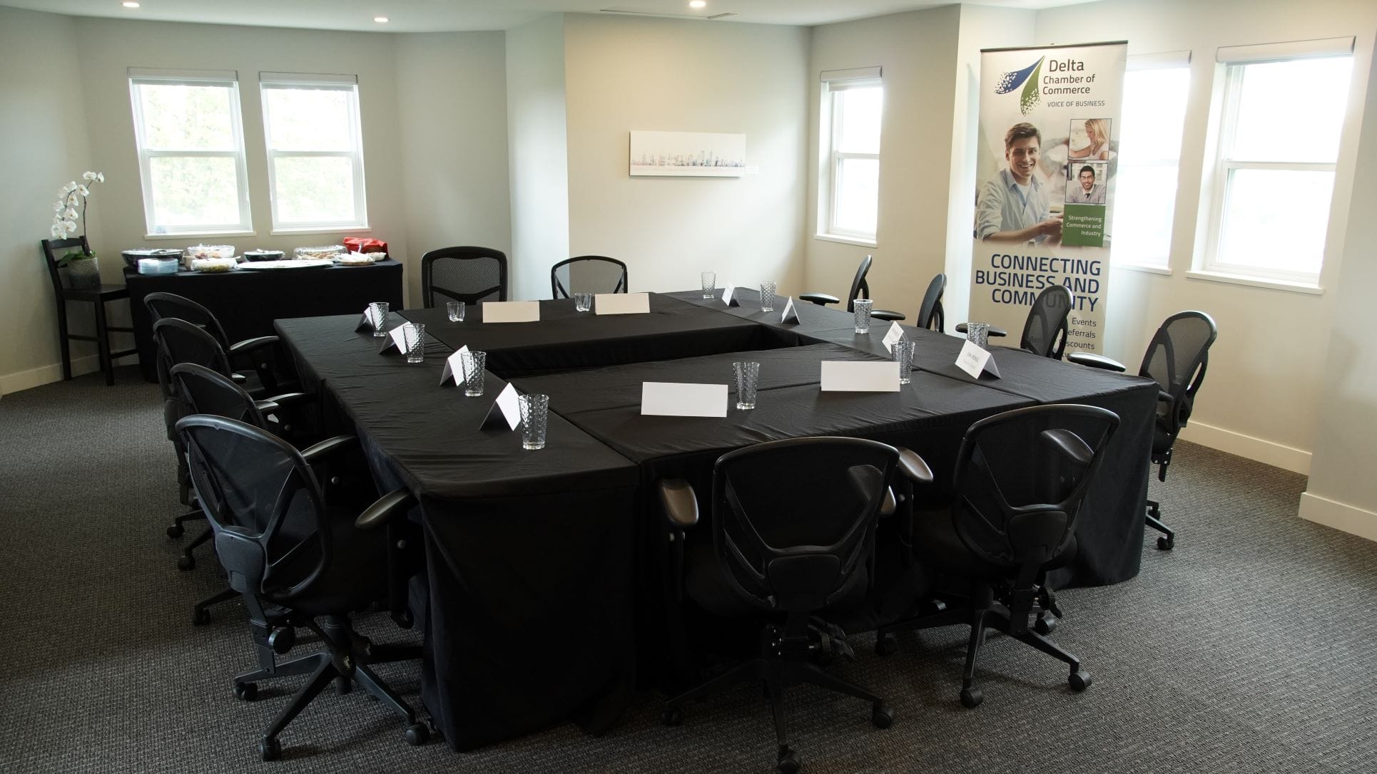A photo of the DCC meeting room space which shows a West-facing view of the room, with tables set up in a square configuration to accommodate 10 guests and a table with food.