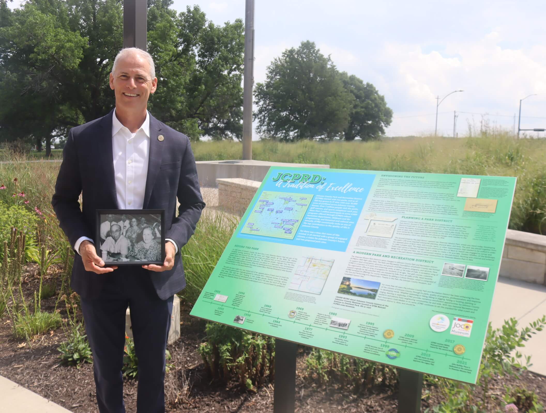 JCPRD Jeff Stewart, Executive Director of JCPRD, holding a photo of John and Marguerite Barkley from the Shawnee Mission Sertoma Club picnic (1961) at the John Barkley Plaza.