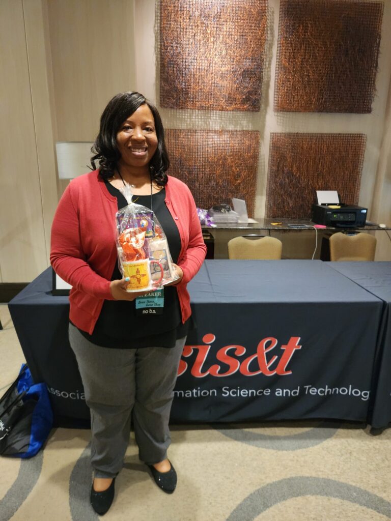 Conference attendee / raffle winner holding a cellophane-wrapped collection of New Mexico-themed goodies in front of a conference table.