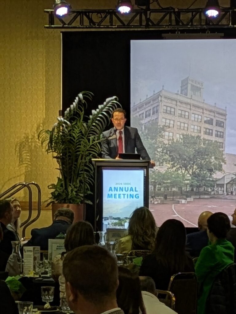 Man standing at podium speaking to group of people at SBDC Annual Meeting