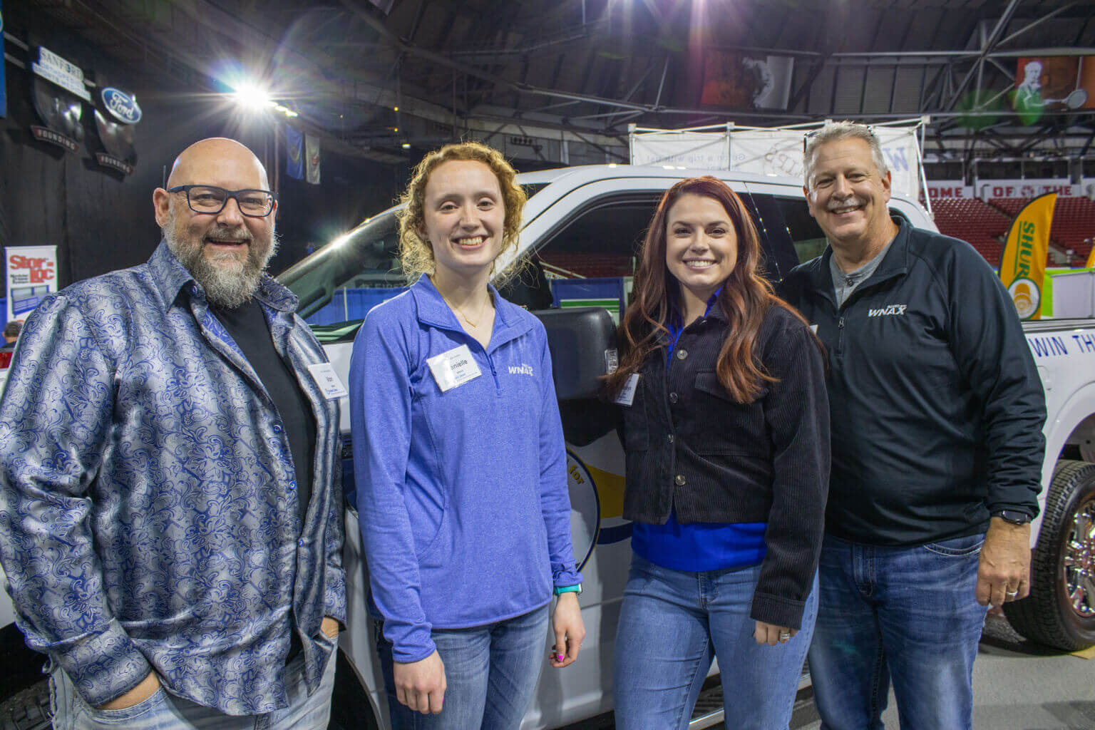 Four people pose in front of a truck at the Dakota Farm Show