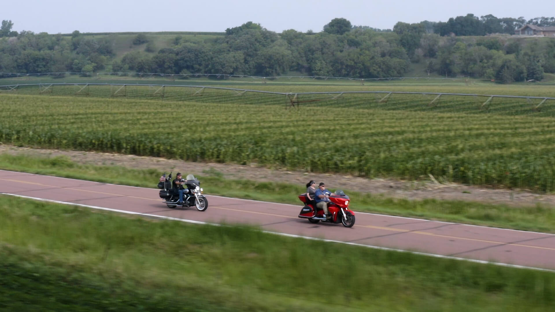 Two bikers riding in rural South Dakota -- by corn fields.