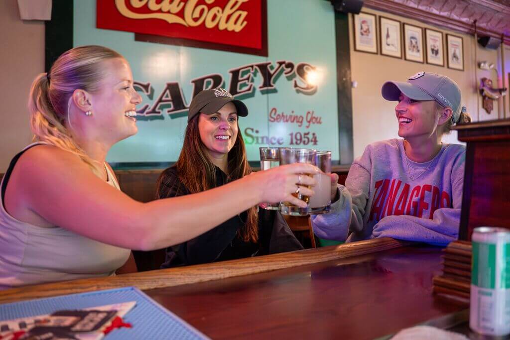 Three people touch glasses in a "cheers' at Carey's Bar in Vermillion