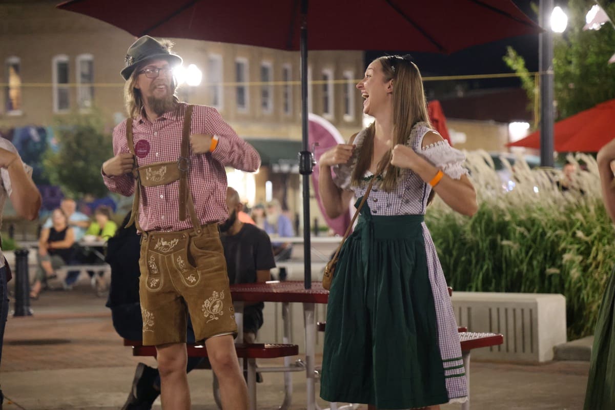 Two people, wearing lederhosen and a dirndl, laughing and dancing.