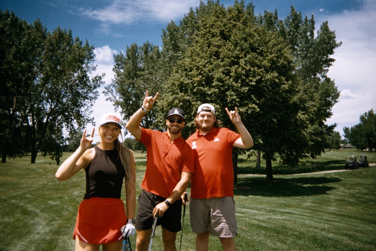 Three people in athletic gear smiling and making a coyote gesture.