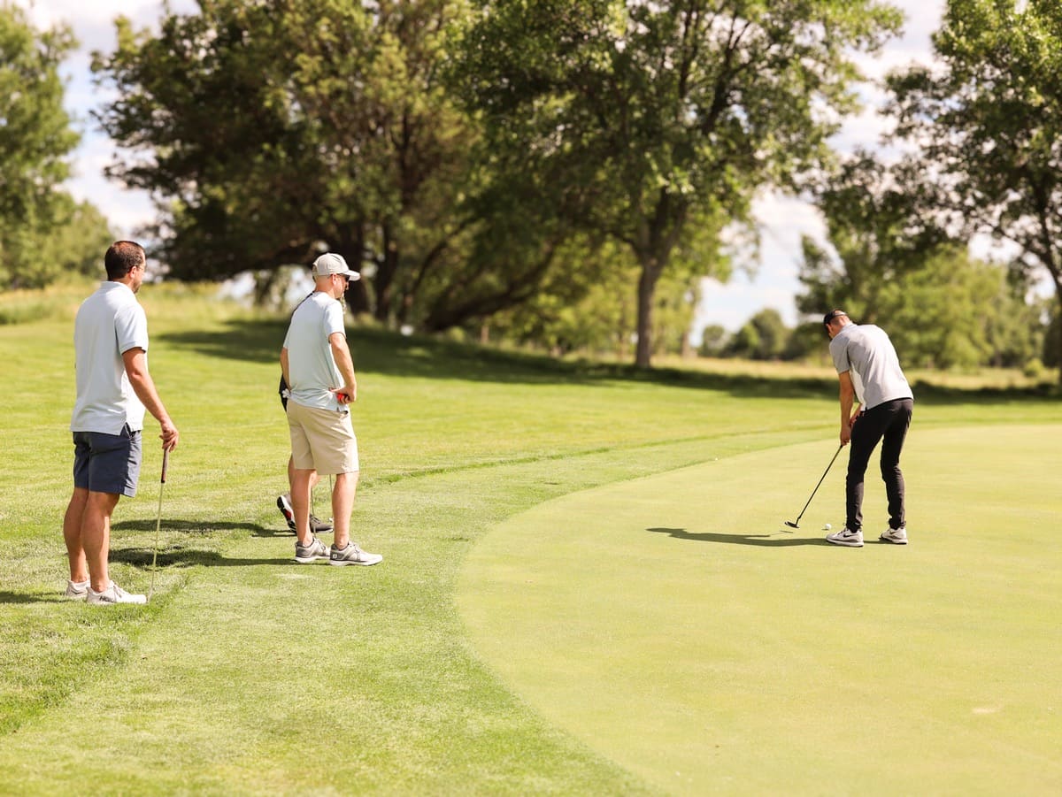 A person preparing to hit a golf ball, with three other people watching and holding clubs.