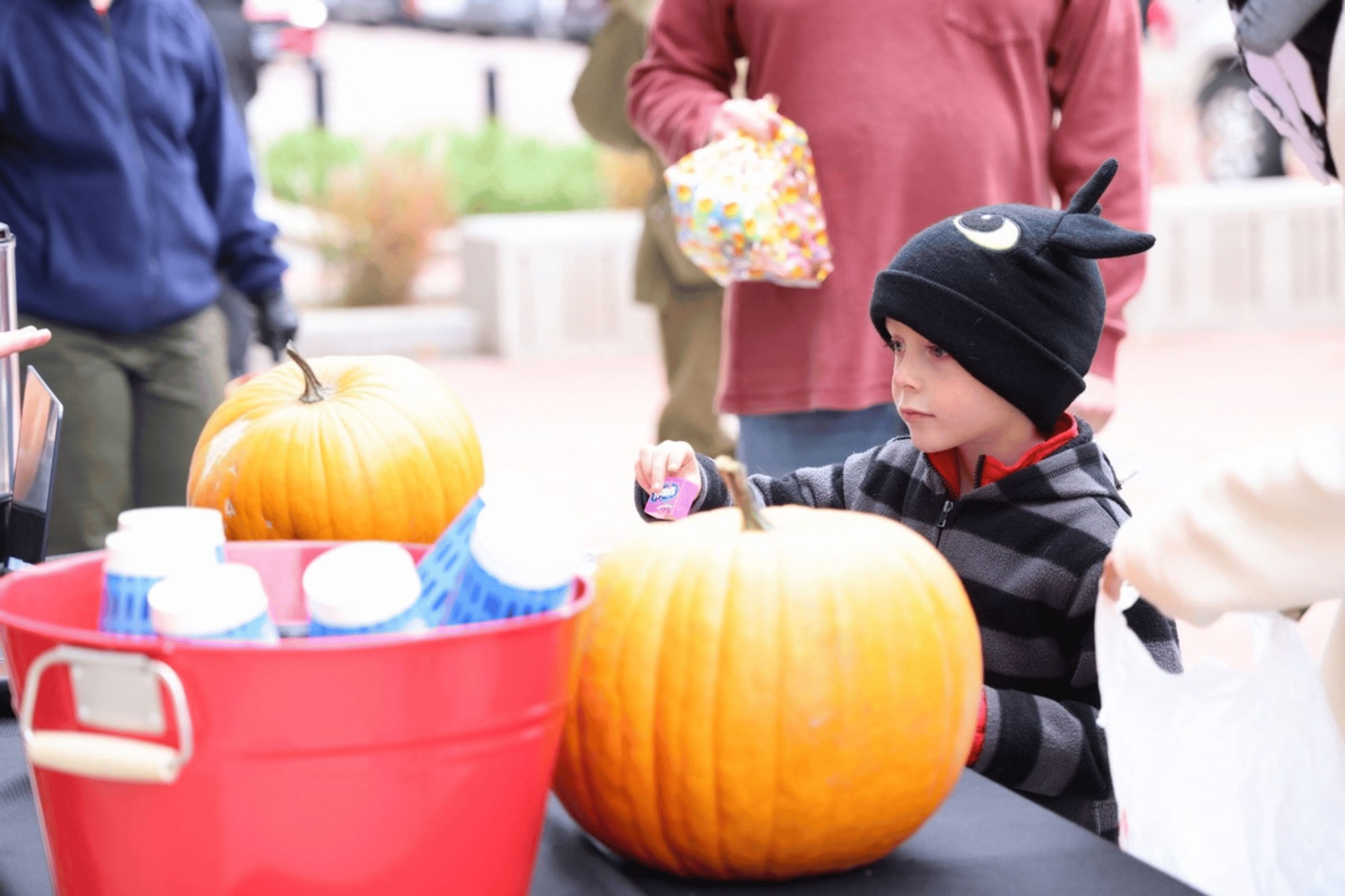 A small child wearing a red and black Halloween costume picks up a piece of candy from a table.
