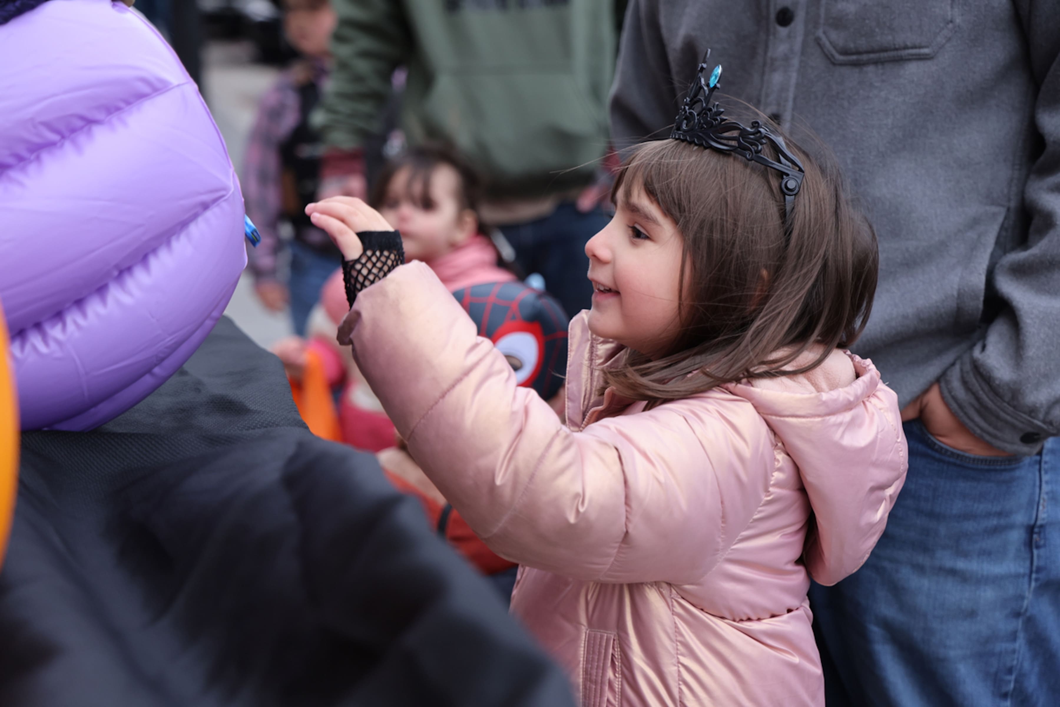 A child wearing a winter coat and crown reaches towards a basket.