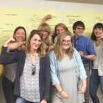 A group of individuals who participated in one of the Nonprofit Credential courses, flexing their arms and smiling in front of notes from the course.