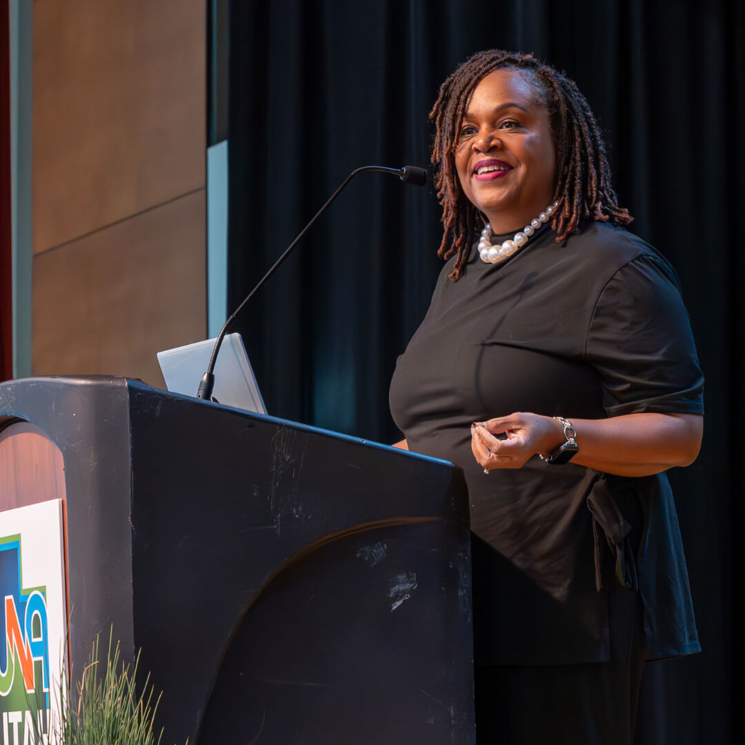 Donna Murray-Brown standing at the UNA mainstage podium, smiling and about to present.