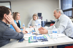 Advanced manufacturing industry leaders tackle challenges through discussion at an Industry Sector Partnership Meeting. Four individuals sit at a table in discussion.