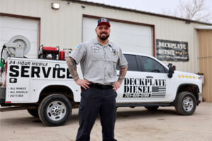 Josh Seley, Owner of Deckplate Diesel, stands in front of a white pickup that says "Deckplate Diesel," along with other promotional text on the side. This is in front of the Deckplate Diesel building in Fargo, ND.