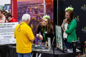 Apex hosts a booth at Business After Hours - Two women standing at a booth talking to an attendee, promoting their business