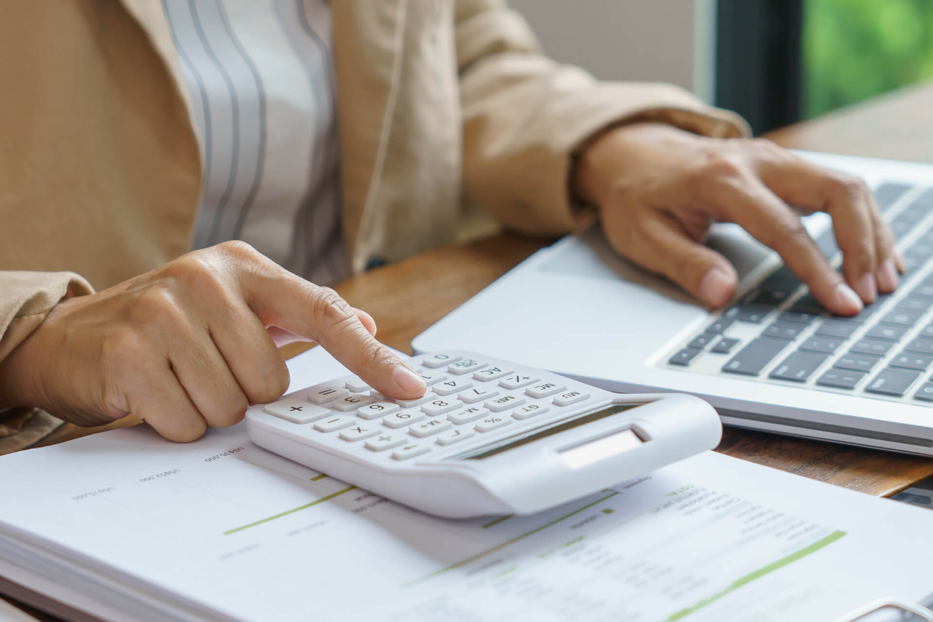 Minnesota Paid Family and Medical Leave Premiums, Taxes and Employer Costs Close-up of a person calculating Minnesota Paid Family and Medical Leave costs using a calculator and laptop at a desk.