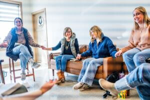 Women sit around a room smiling and laughing as they discuss Healing for High-Achieving Women