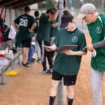 Players in green jerseys check the lineup outside the dugout
