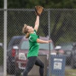 An outfielder reaches up to catch a fly ball