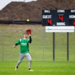 An outfielder tracks a fly ball in front of the scoreboard