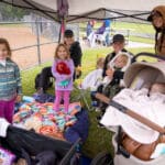 Families and young kids gather under a canopy along the sideline