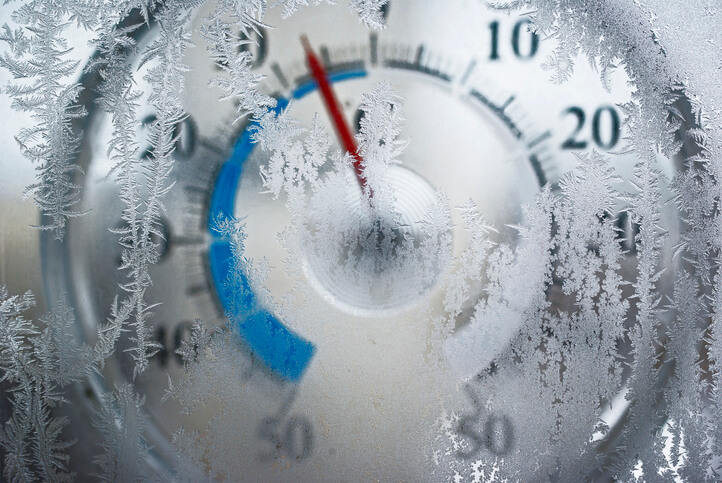 Thermometer for icy window shows the temperature of - 6 degrees Celsius. Red arrow on a blue field. The image is slightly blurry. Frost on the window in focus.