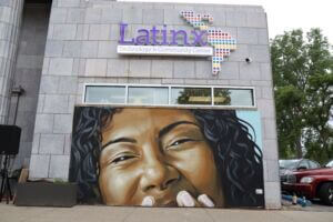 A photo of the mural outside of the Latinx Technology & Community Center. Mural depicts the top-half of a woman's joyful face.