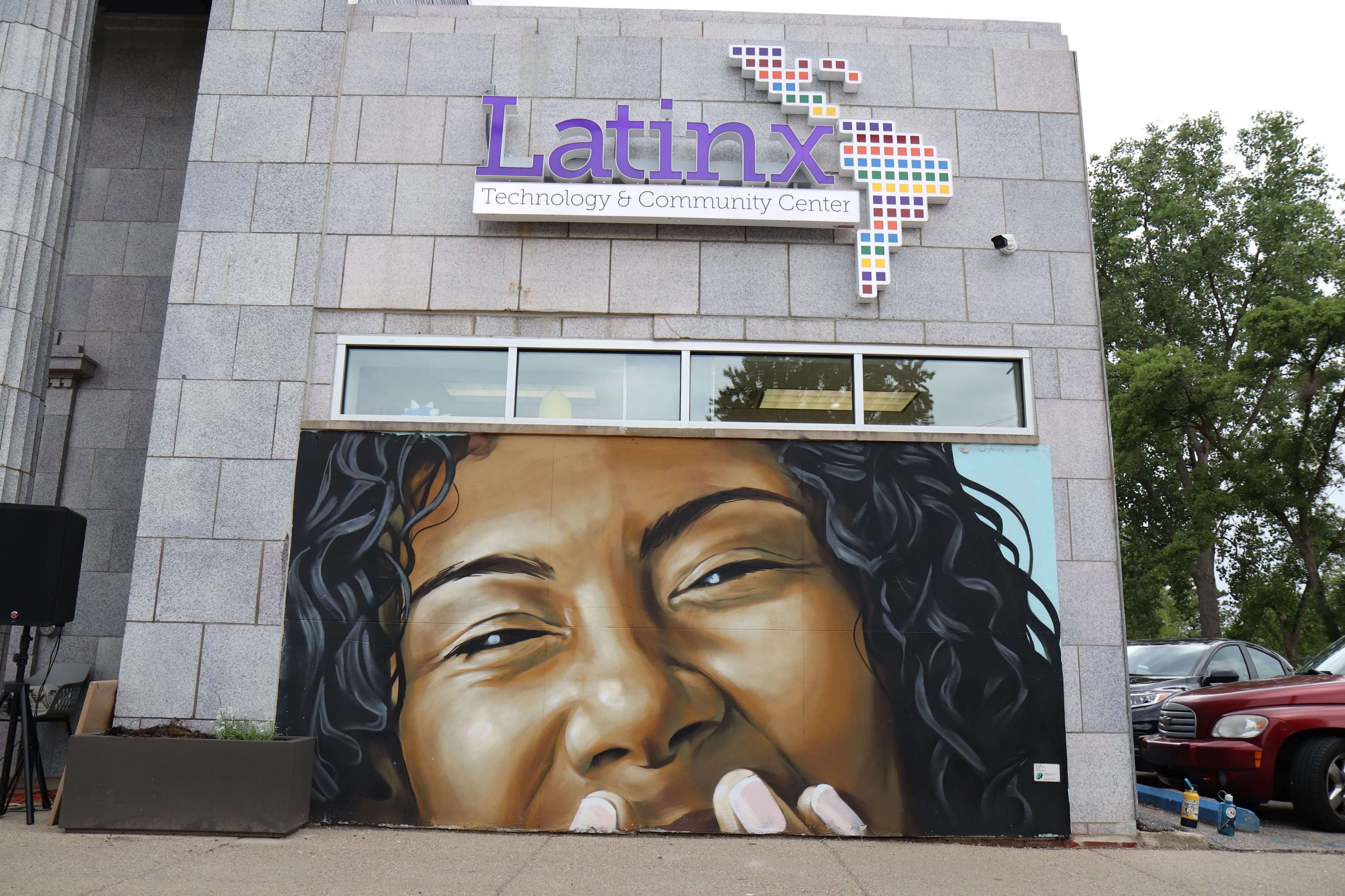 IMG_9098 A photo of the mural outside of the Latinx Technology & Community Center. Mural depicts the top-half of a woman's joyful face.