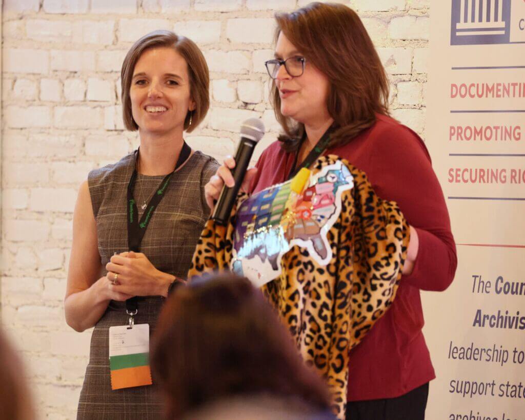 Catheryne Popovitch, incoming CoSA President, and Jami Awalt, outgoing CoSA president, exchanging a leopard print cape