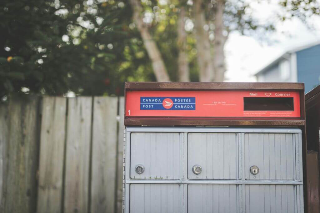 Canada Post mailbox with a fence and tree in the background.