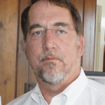 Mark Mazz Mark has a gray goatee and is wearing glasses and he is wearing a white shirt