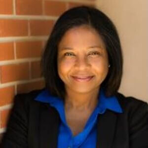Carol Reagan Carol is grinning and has medium length black hair and is wearing a blue shirt and black jacket