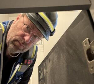 John Torkelson Headshot John is wearing a construction hat and a safety vest and is shown looking into a cabinet