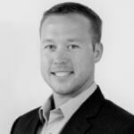 Monochrome photo of Josh wearing a dark suit jacket over a light colored button-up shirt